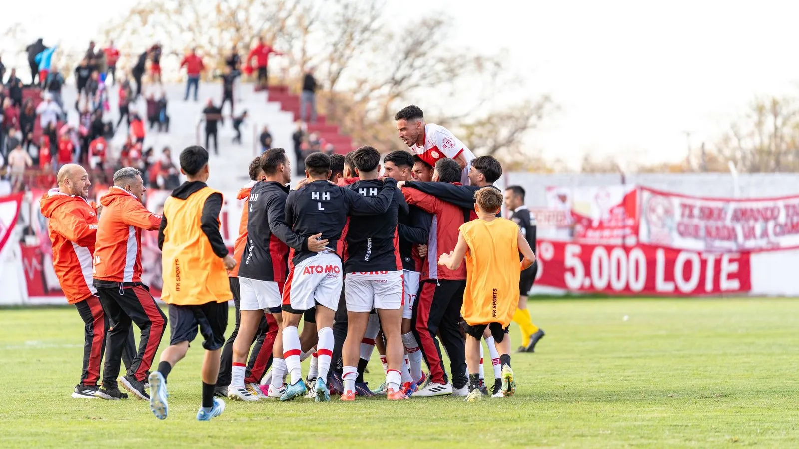Jucători de fotbal care sărbătoresc împreună o victorie pe un teren în aer liber.